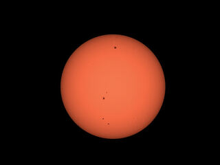 The orange disk of the sun with several dark sunspots